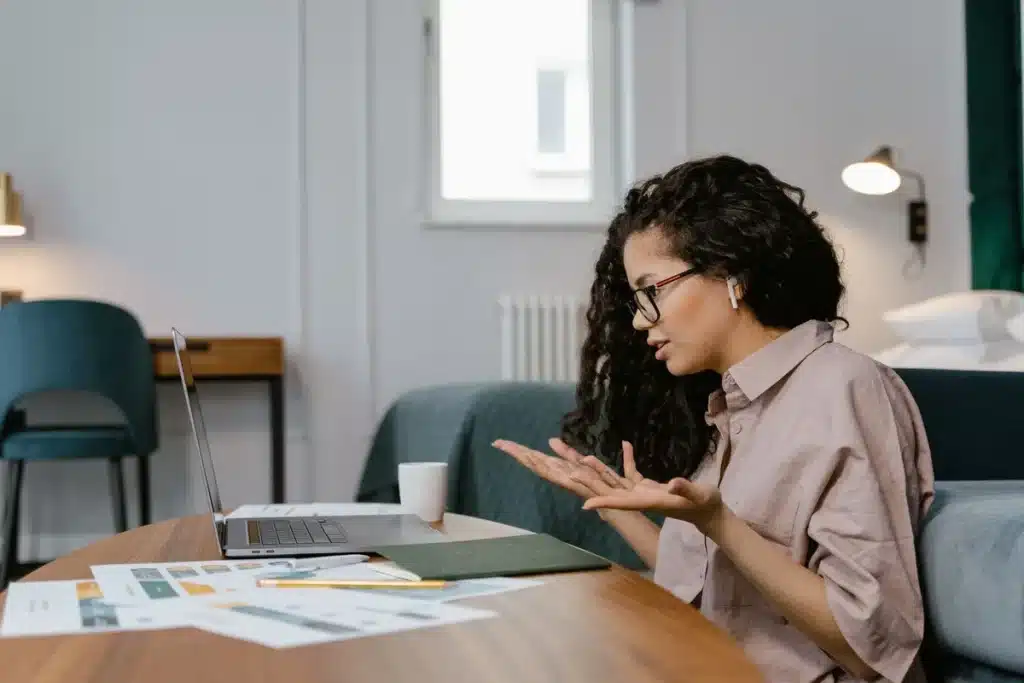 Personne à son bureau avec un ordinateur portable, faisant un geste de pause, lumière naturelle et plante verte en arriè