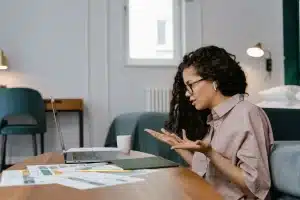 Personne à son bureau avec un ordinateur portable, faisant un geste de pause, lumière naturelle et plante verte en arriè