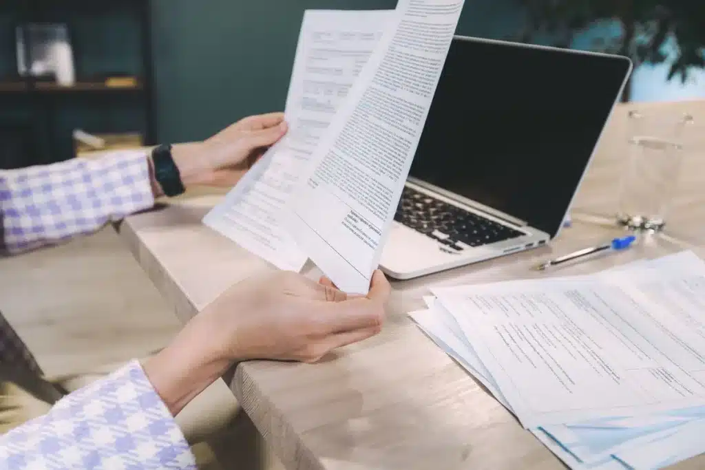 Personne examinant un rapport de crédit sur un bureau avec documents et ordinateur portable