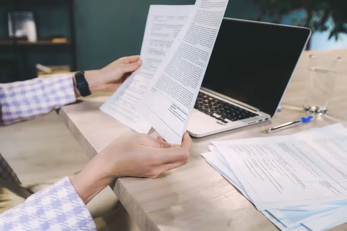 Personne examinant un rapport de crédit sur un bureau avec documents et ordinateur portable