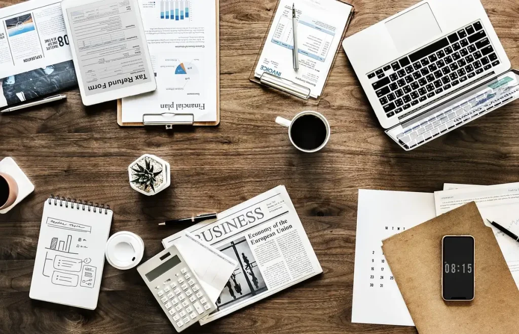 Mains pointant un graphique boursier imprimé sur un bureau en plein jour, ordinateur et tasse de café en arrière-plan fl