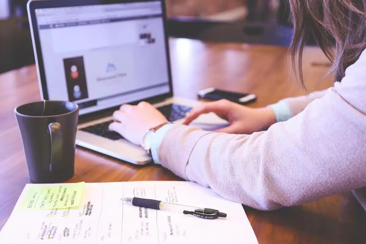 Mains anonymes sur un bureau en pleine journée, ordinateur et carnet visibles