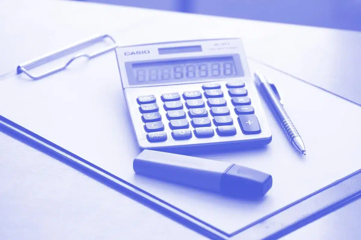 Main anonyme sur un bureau avec documents financiers et calculatrice, lumière du jour