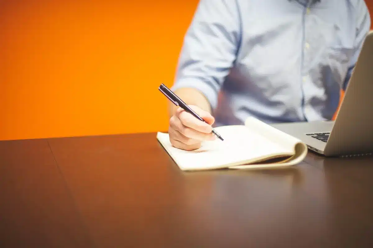 Personne consultant un planning et un ordinateur portable près d'une fenêtre ensoleillée