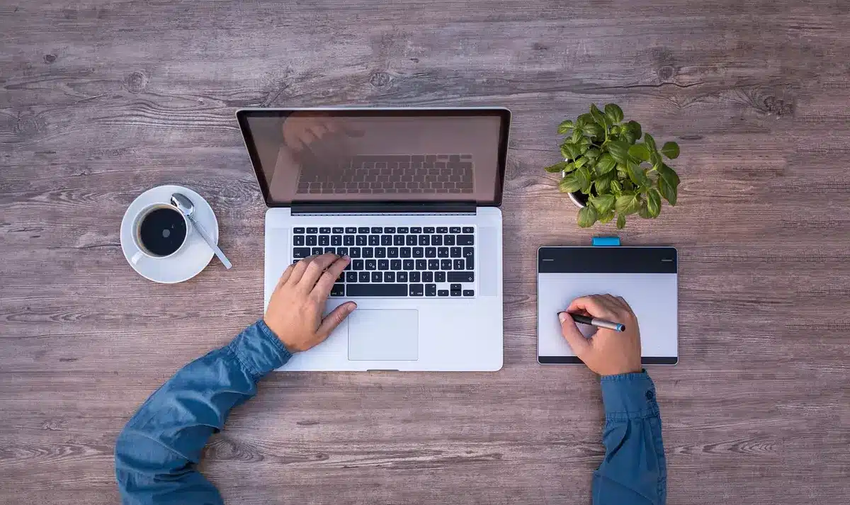 Bureau ensoleillé avec ordinateur portable, documents techniques et mains anonymes travaillant